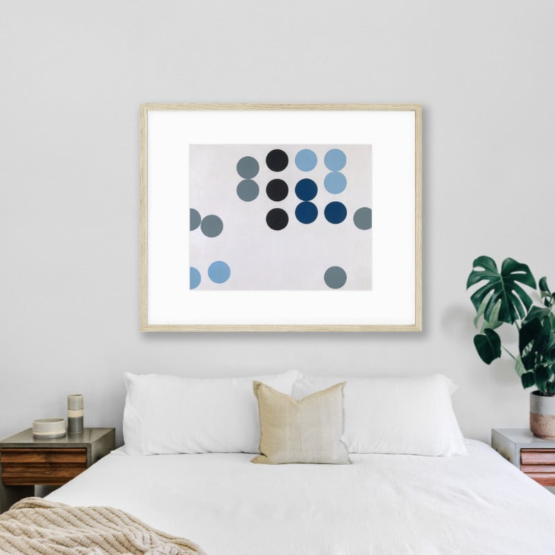 abstract blue dots artwork in natural wood frame hanging on wall above bed